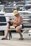 Un hombre sin camisa en el paseo marítimo de Brighton Beach lee dos libros.