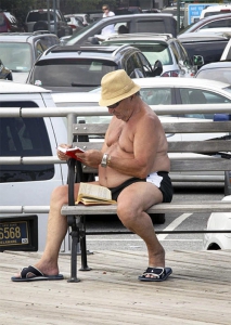 Un hombre sin camisa en el paseo marítimo de Brighton Beach lee dos libros.